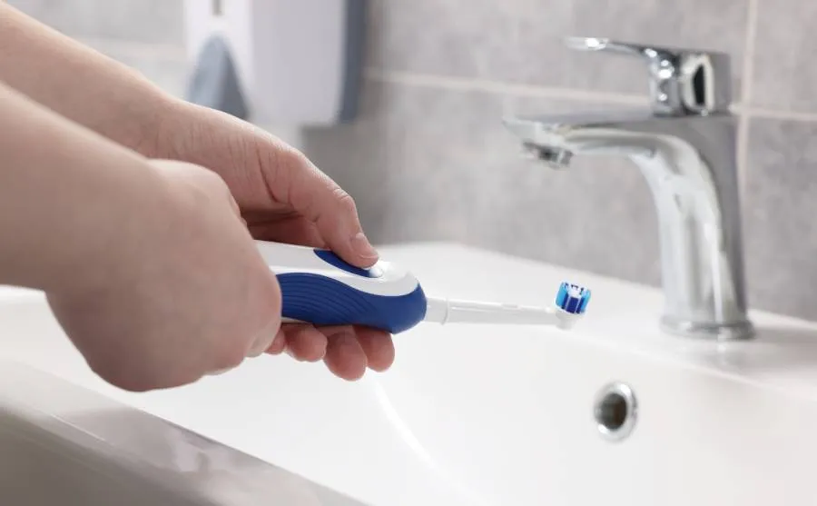 Frau hält Oral-B Zahnbürste über Waschbecken