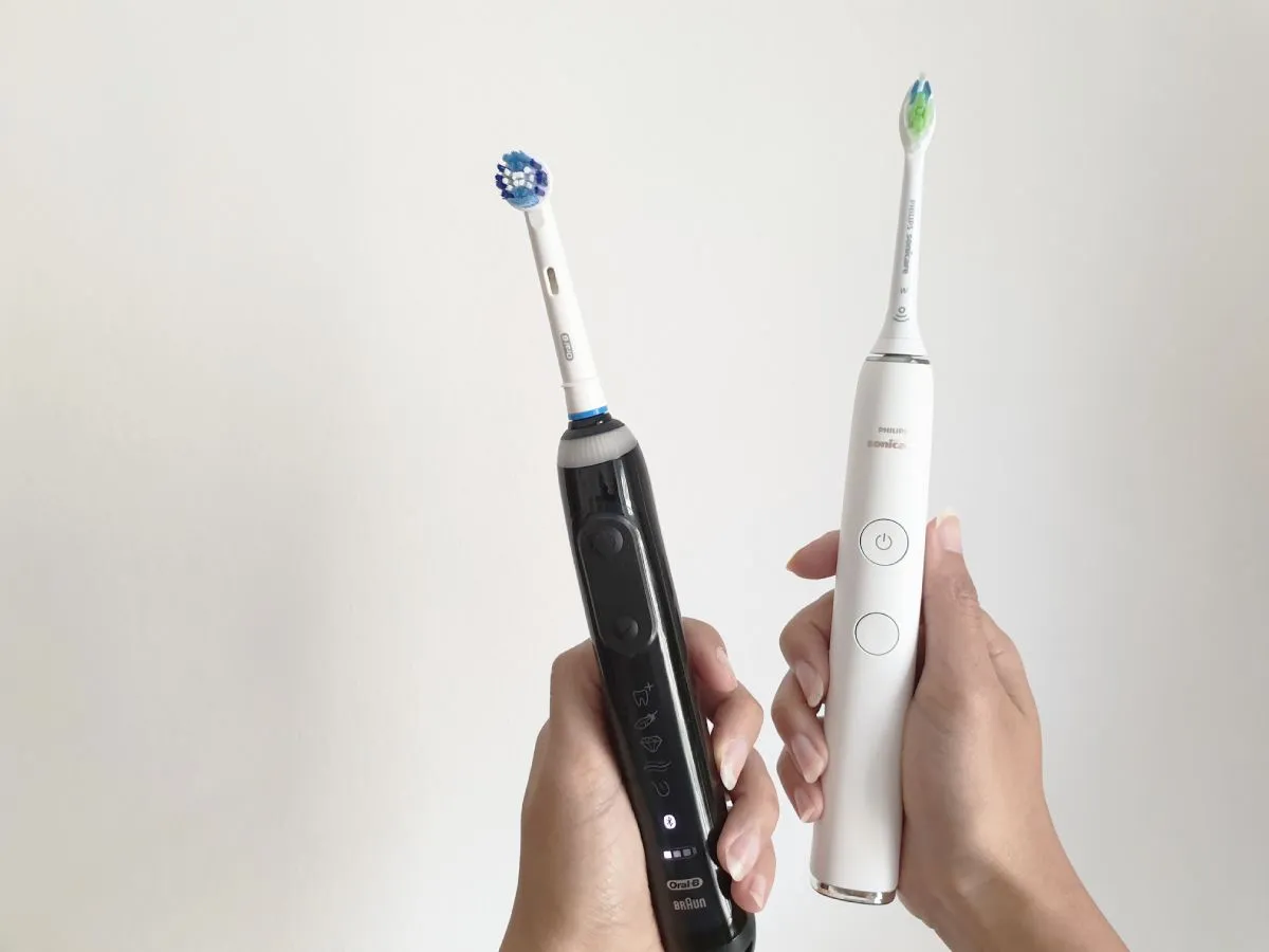 oral-b zahnbürste und sonicare zahnbürste in jeweils einer hand